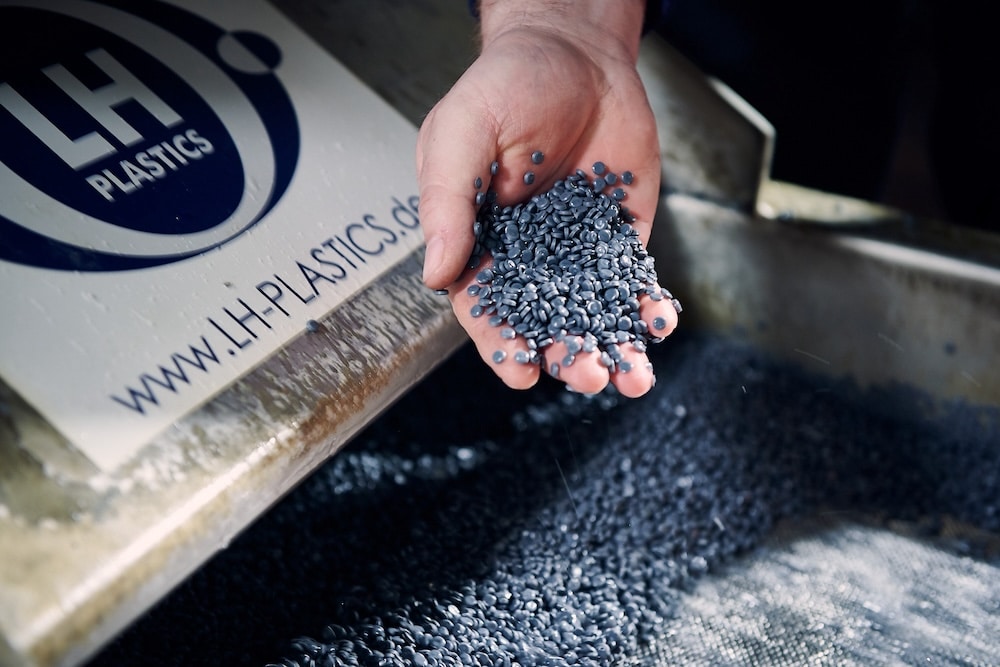 dunkelgraues Regranulat wird von einer Hand aus der Produktion gefangen und präsentiert. Bild: LH Plastics