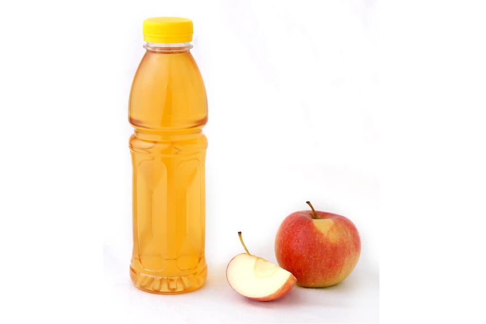 Apfelsaft in PET-Flasche. Neben der Mehrwegflasche liegt ein Apfel.