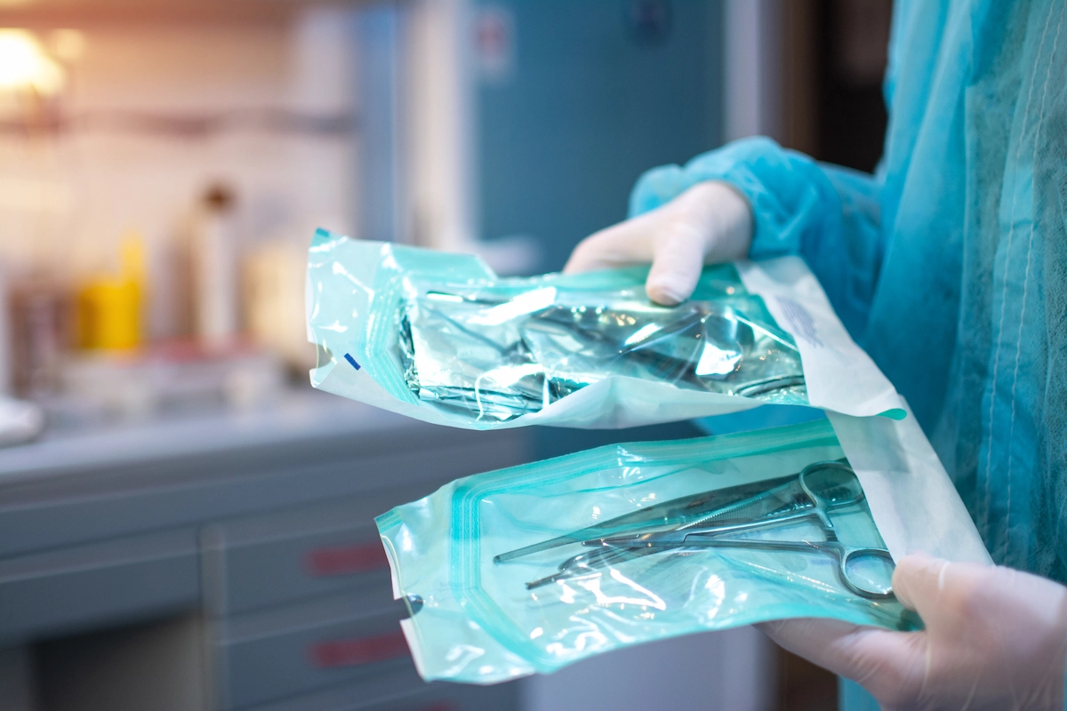 Nahaufnahme von Zahnarzthänden in weißen sterilen Handschuhen mit zahnärztlichen Werkzeugen für den chirurgischen Einsatz verpackt in einer Schutzfolie aus Kunststoff.