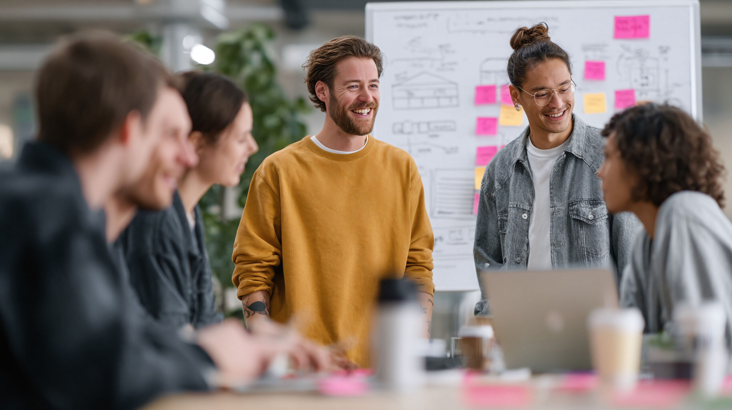 Kreative Fachkräfte arbeiten in einem modernen Büro zusammen. Ein vielfältiges Team entwickelt Ideen mithilfe eines Whiteboards, Notizen und eines Laptops. Ein Konzept für eine positive, innovative Arbeitskultur.